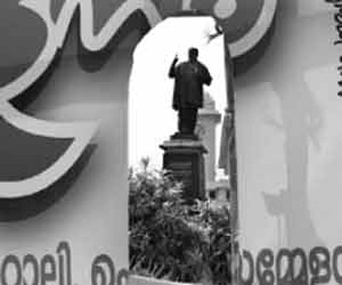 The statue of poet Kumaran Asan in front of the Kerala University Office seen through a ripped political banner placed on the fence.