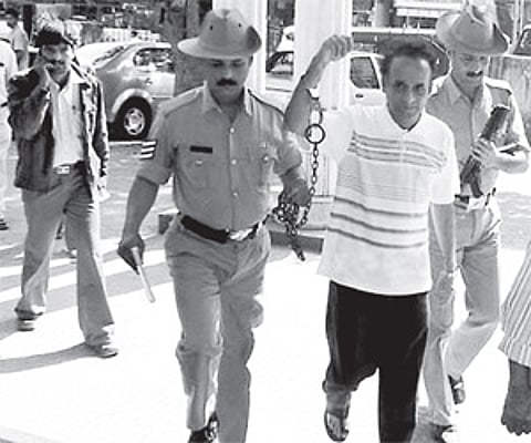 Chitra Publications chairman and journalist B V Seetharam being brought handcuffed to the Udupi court on Monday.