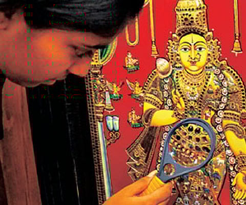 A girl checking out intricate work on a Tanjore painting using a magnifying glass. The painting was made by Sarboji Raja Bhonsle.