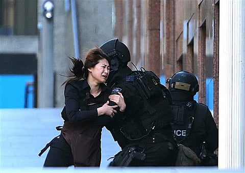 A hostage runs to armed tactical response police officers for safety after she escaped from a cafe under siege at Martin Place in the central business district of Sydney, Australia, Monday | AP
