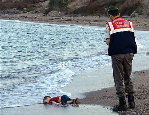 Paramilitary police officers investigate the scene before carrying the lifeless body of an unidentified migrant child, lifting it from the sea shore, near the Turkish resort of Bodrum, Turkey, early Wednesday, Sept. 2, 2015. | AP