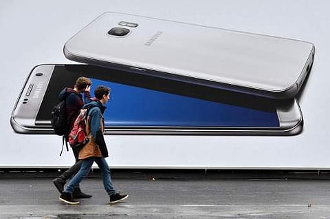 Boys walk past a billboard advertising the Samsung's Galaxy S7 Edge smartphone | AFP