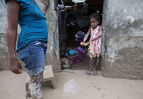 A girl helps her mother to remove mud from her house. (Photo | AP)