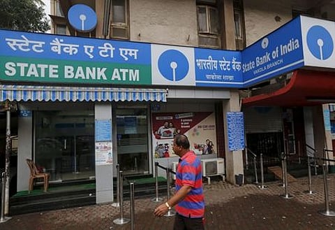 A man walks past an ATM at a State Bank of India branch in Mumbai. | Reuters