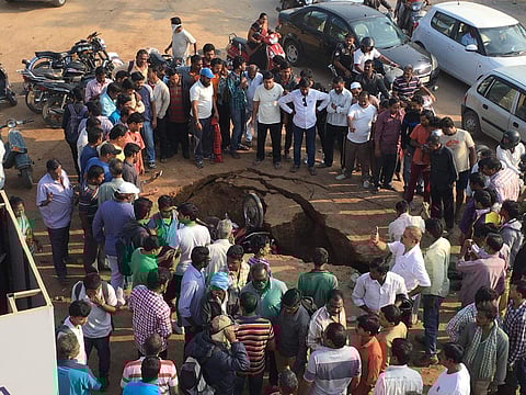 Bystanders gather round to watch after two motorcycles fell into a sink hole after a road caved in at Safilguda, a suburb of Hyderabad. | EPS