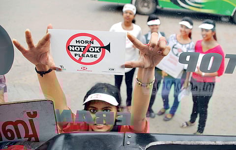 (Representational image) A student pasting ‘No Horn Day’ sticker on a bus to create awareness about noise pollution.