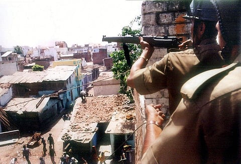 A policeman takes aim with his rifle from the roof of a building as a mob riots down in the streets below in Ahmedabad, 22 April 2002. (File Photo | AFP)