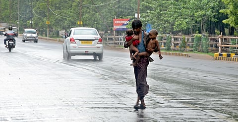 A man tries to cross a road with his children in the sudden downpour that lashed Bhubaneshwar.