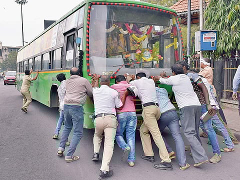 Traffic policemen and public pushing a BMTC bus that broke down near Town Hall on Friday | (Jithendra M |EPS)