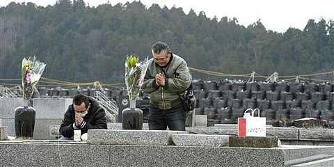 People pray in front of ancestors' grave as black plastic bags containing radiation contaminated waste are piled in the background, in Futaba, Fukushima prefecture, northern Japan. |AP