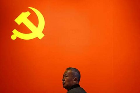 A Chinese man stands near a Communist flag on display . (Photo | AP)