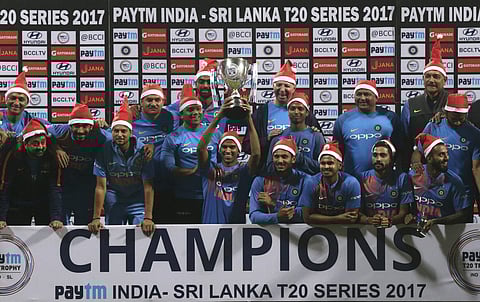 Players and support staff of Indian cricket team sport Santa caps as they pose with the winners trophy after their win in the third T20 against Sri Lanka in Mumbai. | AP