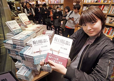 A woman poses with 'Kishidancho Goroshi', book written by Haruki Murakami, at a book store in Tokyo shortly after midnight, Friday, Feb. 24, 2017.