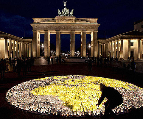 A volunteer of the 'World Wide Fund for Nature' sets the final candles amongst about 5000 candles to picture the globe prior to 'Earth Hour' in front of the Brandenburg Gate in Berlin. (File photo | AP)