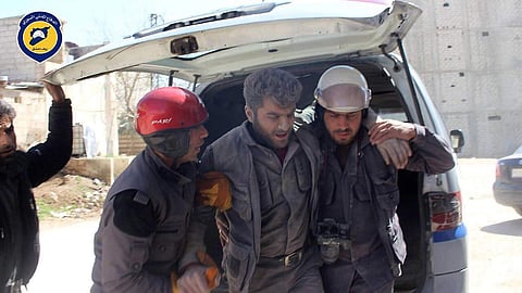 In this photo provided by the Syrian Civil Defense group known as the White Helmets, Civil Defense workers help their teammate after airstrikes hit a main street, killing many people, activists said, in the Damascus suburb of Hamouriyeh, Syria, Saturday,