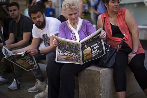 A woman reads a newspaper reporting in the front about the suicide attack at a concert by Ariana Grande and in the back page about the victory of Manchester United winning the soccer Europa League final, before holding a minute of silence in a square in c
