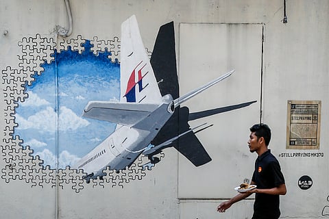 In this Tuesday, Feb. 23, 2016 photo, a waiter walks past a mural of flight MH370 in Shah Alam outside Kuala Lumpur, Malaysia. A Malaysian woman is suing Malaysia Airlines and the government for $7.6 million in damages over the loss of her husband on Flig