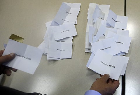 A voting station volunteer holds a ballot for Emmanuel Macron as they count ballots, Sunday, May 7, 2017 in La Penne sur Huveaune, near Marseille, southern France. (AP)