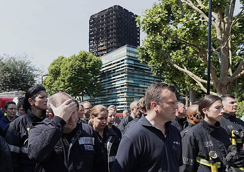 Emergency services workers take part in a minute's silence in front of Grenfell Tower in London, Monday, June 19, 2017. Tens of people died when a fire engulfed the high-rise apartment block in west London last week. (AP Photo/Kirsty Wigglesworth)