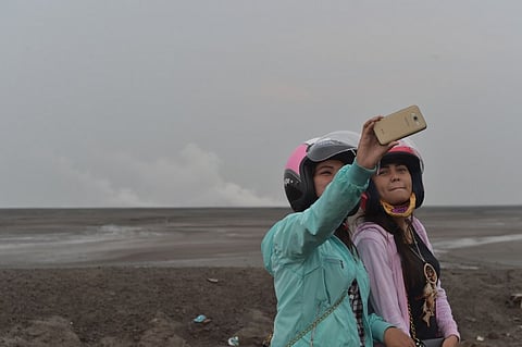 Two Indonesian tourists taking selfies at a mud volcano area in Sidoarjo, East Java. (AFP)