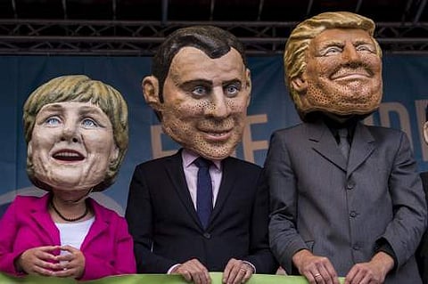 Performers wearing masks of (L-R) German Chancellor Angela Merkel, French President Emmanuel Macron and US President Donald Trump hold a placard reading: 'Better off equal! close the gap between rich and poor' during a demonstration called by several NGOs