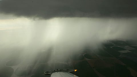 A wing-mounted generator emits particles of silver iodide as circular fields of crops are seen in the distance.