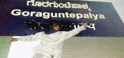 A Metro employee cleaning a blackened name board at Goraguntepalya Metro station in Bengaluru on Thursday. | Jithendra M