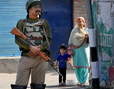 A woman and her son look on as a security guard stands at a block road during strict curfew imposed on the first death anniversary of Hizbul Mujahideen commander Burhan Wani in Srinagar on Saturday.