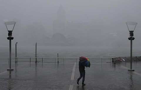 A man holds an umbrella against the strong wind caused by tropical storm Pakhar on the waterfront of Victoria Habour in Hong Kong on Sunday. (Photo | AP)
