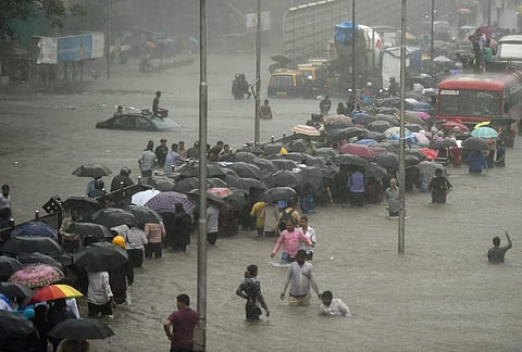 People walk along a flooded street during heavy rain showers in Mumbai on Tuesday. | PTI