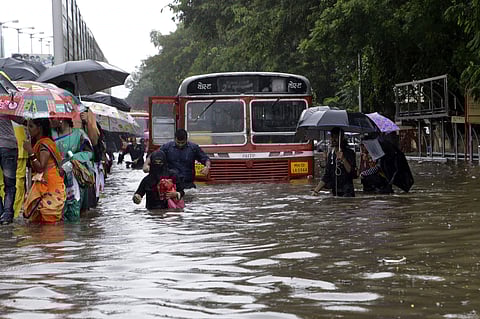 People wade next to vehicles during a traffic jam along a flooded road during heavy rain showers in Mumbai. (Photo | AP)