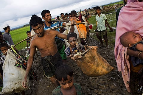 A Rohingya ethnic minority refugee from Myanmar carries a child in a sack and walks through rice fields after crossing over to the Bangladesh side of the border near Cox's Bazar's Teknaf area, Friday, Sept. 1, 2017. | AP