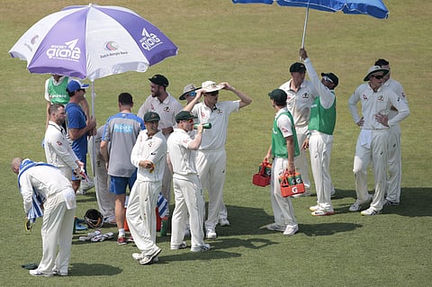 Australian players take shelter under umbrellas during the drinks break on the first day of their second test cricket match against Bangladesh in Chittagong, Bangladesh. | AP