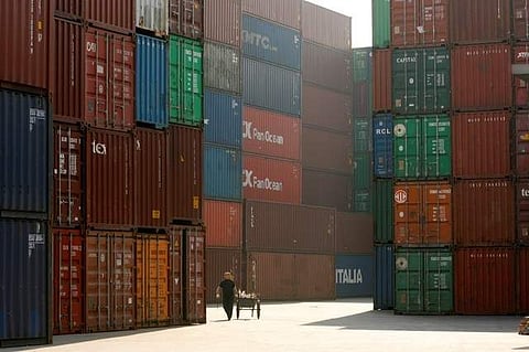 A woman walks past containers at a port in Shanghai. | REUTERS