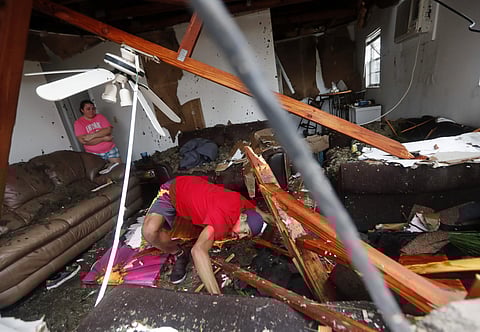 Dorian Carter looks under furniture for a missing cat after several trees fell on their home during Hurricane Michael in Panama City, Fla., Wednesday, Oct. 10, 2018.