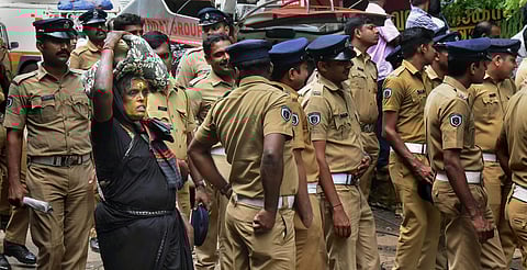 An elderly woman on her way to Sabarimala Temple as police personnel stand on guard in Pathanamthitta on Wednesday. (Photo | PTI)