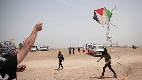 Palestinian protesters fly a kite with a burning rag dangling from its tail during a protest at the Gaza Strip's border. (Photo | AP)