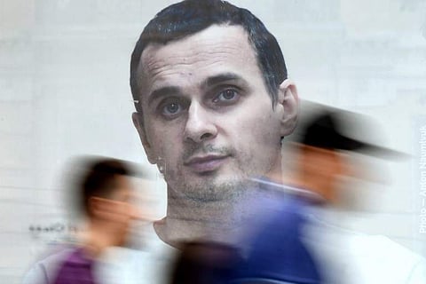 People walk past a poster with a photo of Ukrainian film director Oleg Sentsov, taken by journalist Anton Naumlyuk, and displayed in a shop window in the center of Kiev on July 5, 2018. Oleg Sentsov, who has been on hunger strike for over 50 days in a rem