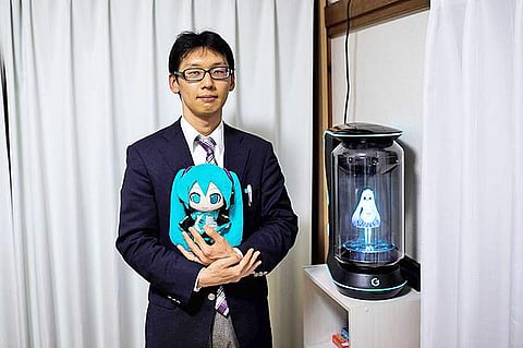 Akihiko Kondo poses next to a hologram of Japanese virtual reality singer Hatsune Miku as he holds the doll version of her at his apartment in Tokyo, a week after their wedding. (Photo | AFP)