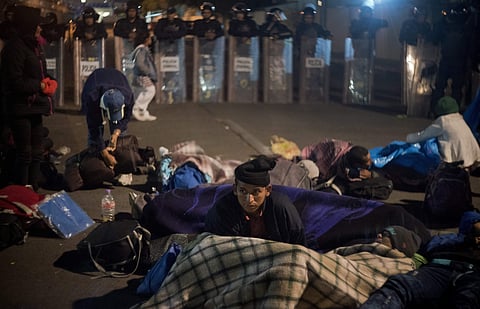 A migrant get ready to spend the night in front of a line of Mexican police in riot gear at the Chaparral border crossing in Tijuana, Mexico. (Photo: AP)