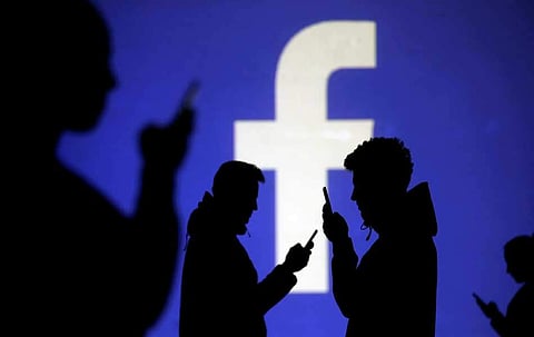 Silhouettes of mobile users are seen next to a screen projection of Facebook logo in this picture illustration taken March 28, 2018. (File Photo |Reuters)