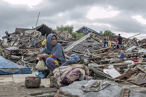 A tsunami survivor sits on a pice of debris as she salvages items from the location of her house in Sumur, Indonesia, Monday, Dec. 24, 2018. (Photo | AP)