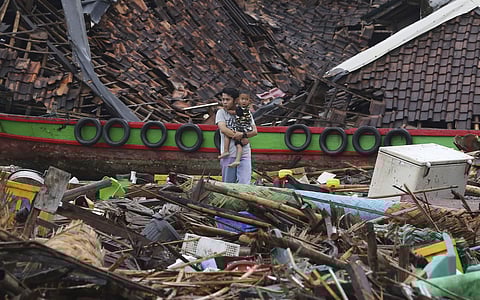 A man holding a child looks the damage at a tsunami-ravaged village in Sumur, Indonesia, Tuesday, Dec. 25, 2018. (Photo | AP)
