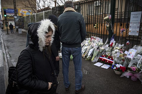 People stand next to flowers placed at the main gate of the police headquarters in Carcassonne. (Photo | AP)