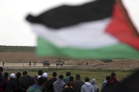 Protesters, one holding a Palestinian flag, stand in front of Israeli soldiers during a demonstration near the Gaza Strip border with Israel, in eastern Gaza City. | File AP