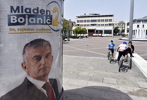People rest near a billboard showing Mladen Bojanic, backed by a diverse group of parties, including a pro-Russian Democratic Front, reading: ''Mladen Bojanic - Yes, together we can'' in Montenegro's capital Podgorica. (AP)
