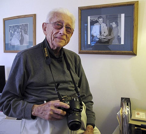 Former Associated Press photographer Gene Herrick poses between two of his most famous pictures at his home in Rocky Mount, Va., on Friday, Feb. 2, 2018. | Associated Press