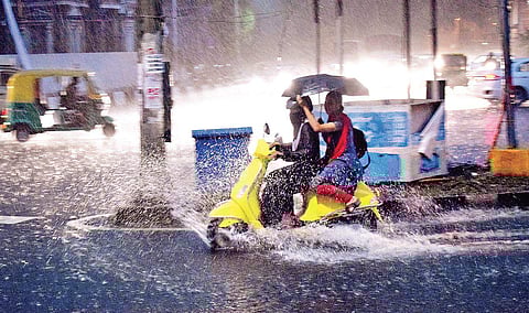 A motorist rides amid rain as the pillion rider struggles to save themselves from getting drenched | pandarinath b