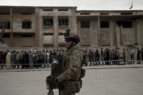 An Iraqi soldier stands guard as voters wait in a long line to cast their ballots in the country's parliamentary elections at a polling site in a damaged building in west Mosul. (AP)