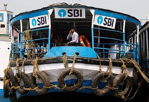 A man speaks on his mobile phone while sitting inside a ferry under the advertisement boards of State Bank of India (SBI), on the bank of the river Ganges in Kolkata. | REUTERS